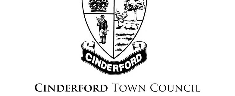Black and white Cinderford Town Council crest featuring a shield with a crown, miner, tree, and stag, above a banner reading "Cinderford." The words "Cinderford Town Council" are below the crest.