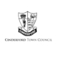 Black and white Cinderford Town Council crest featuring a shield with a crown, miner, tree, and stag, above a banner reading "Cinderford." The words "Cinderford Town Council" are below the crest.